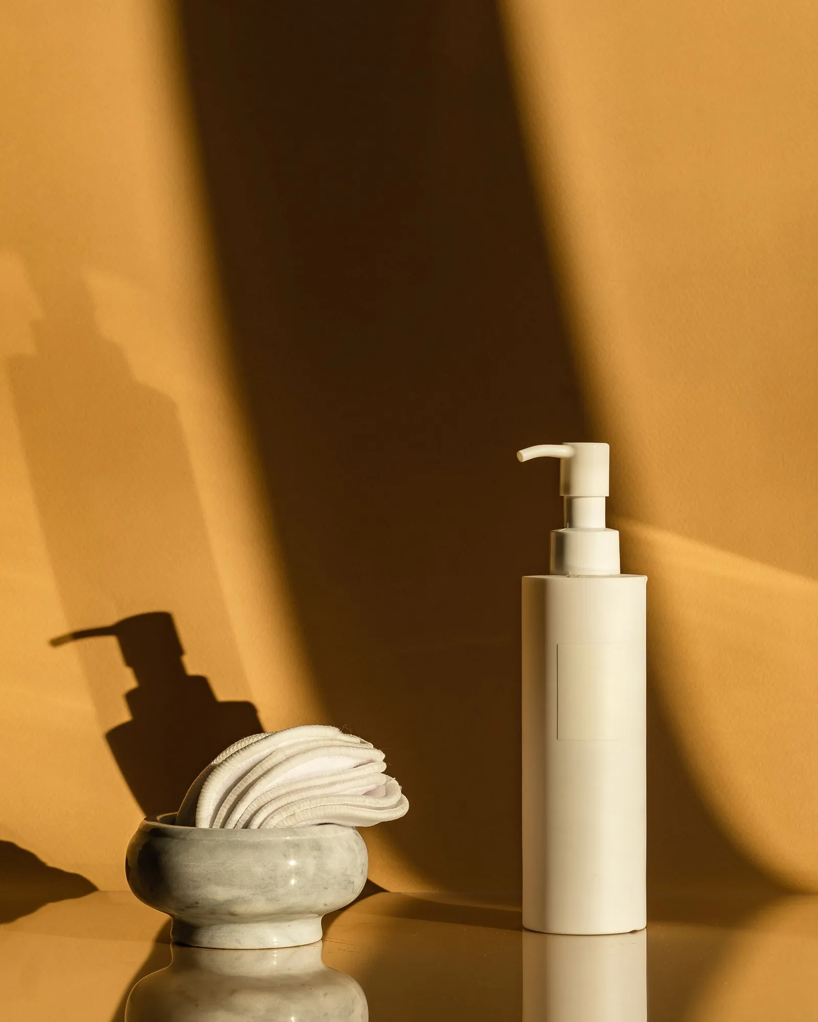 White pump bottle and a marble bowl of cotton pads in warm light