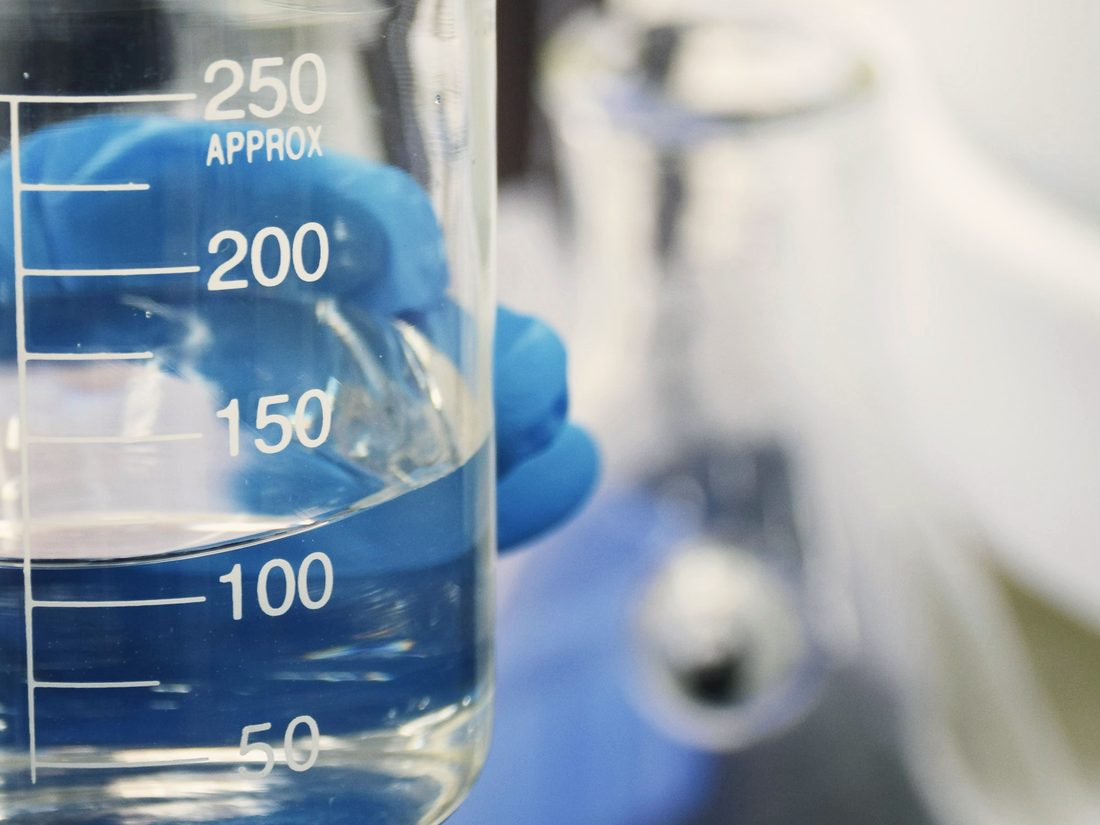Gloved hand holding a graduated glass beaker